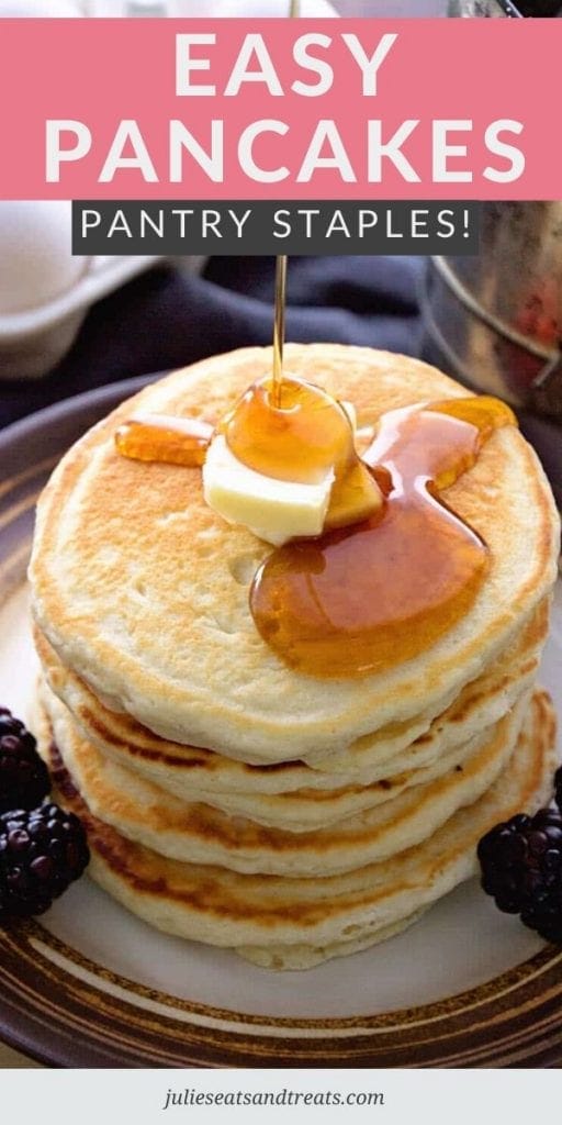 Syrup being poured over a tall stack of pancakes with butter and black berries