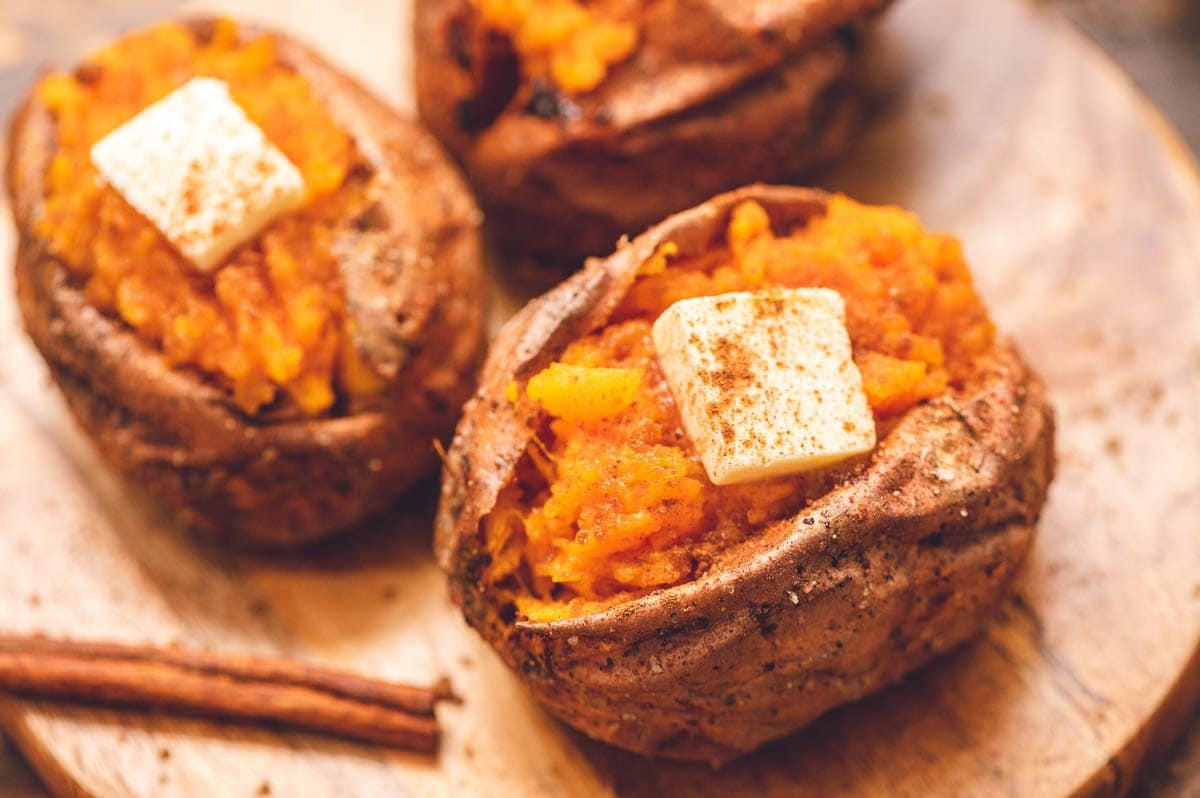 A wooden cutting board with baked sweet potato cut open with slice of butter