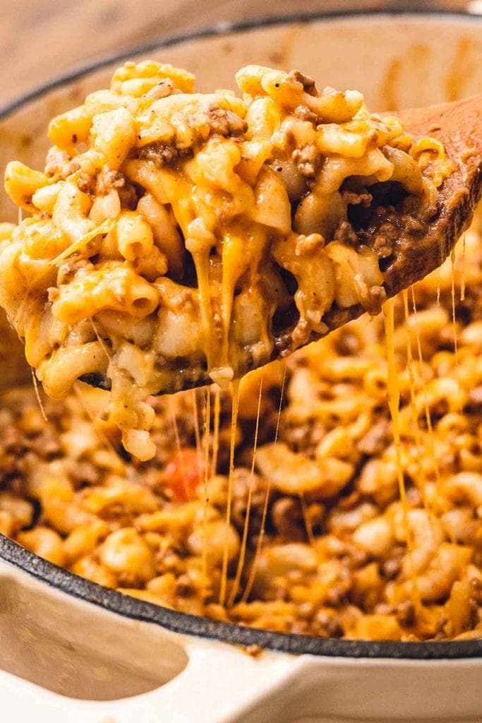 Wooden spoon with cheesy hamburger helper over a dutch oven