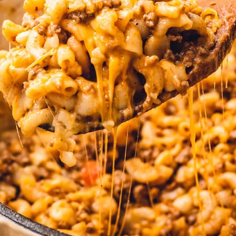 Wooden spoon with cheesy hamburger helper over a dutch oven