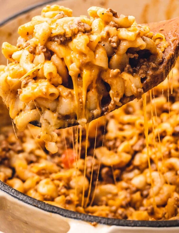 Wooden spoon with cheesy hamburger helper over a dutch oven
