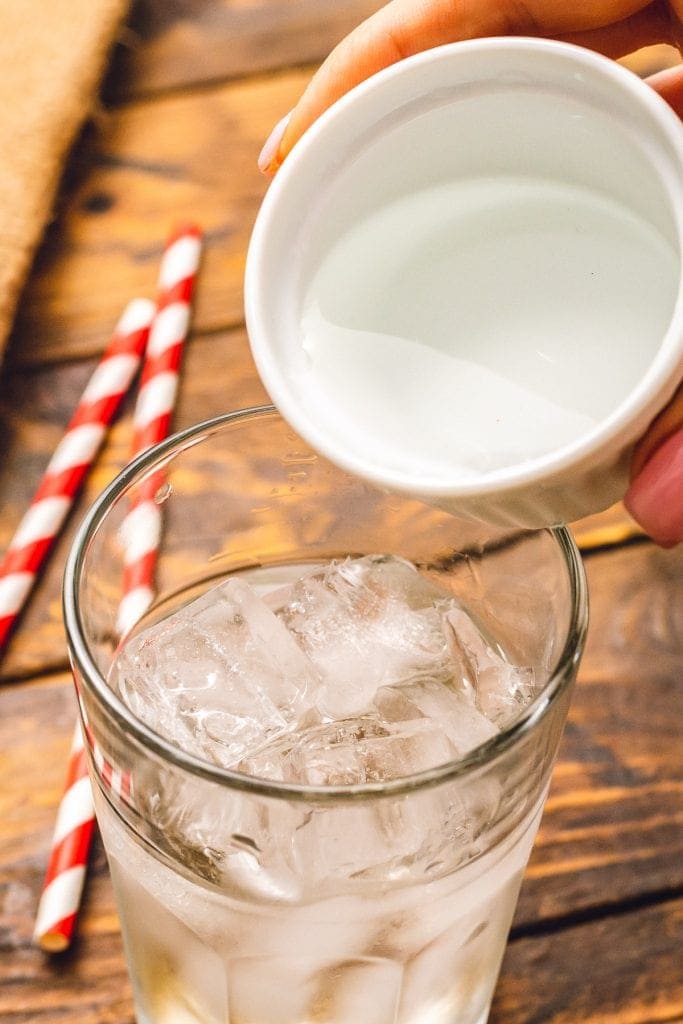 Pouring vodka from white dish into glass with ice