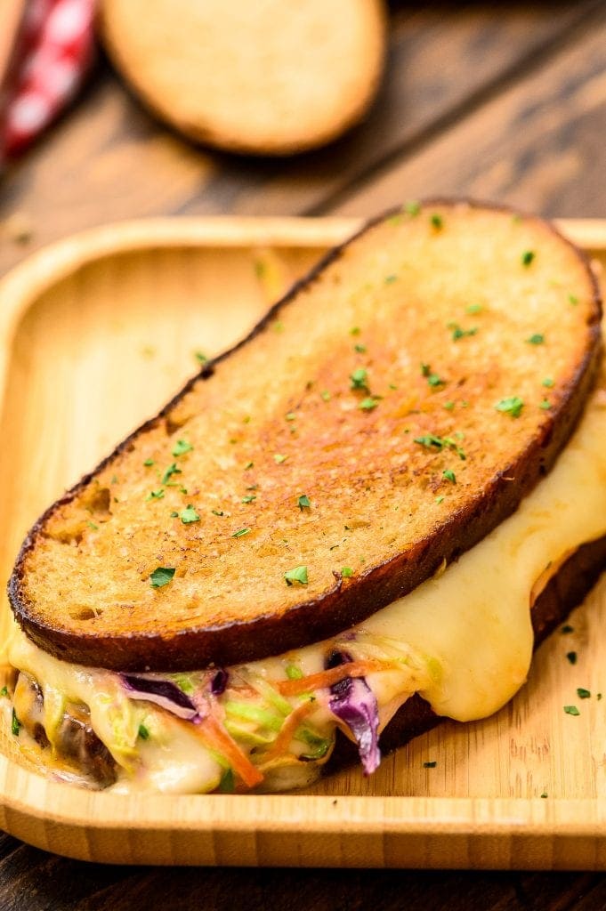 Wood platter with sandwich showing melted cheese and coleslaw