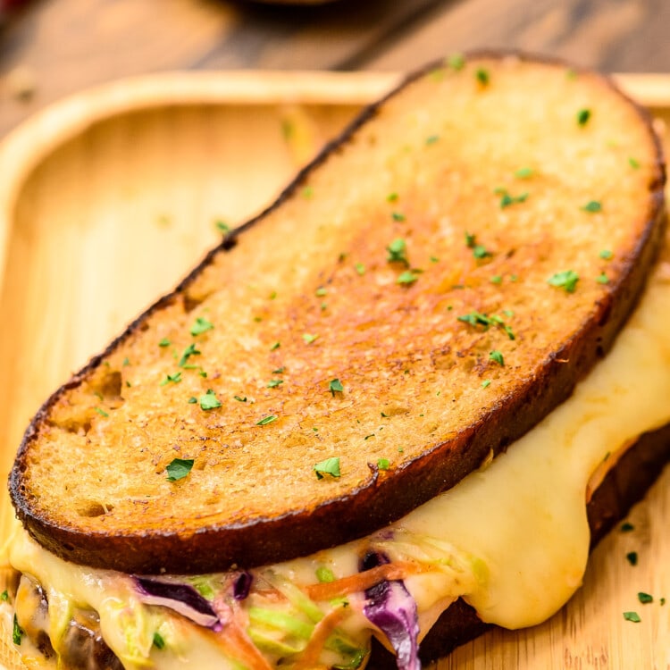 Wood platter with sandwich showing melted cheese and coleslaw