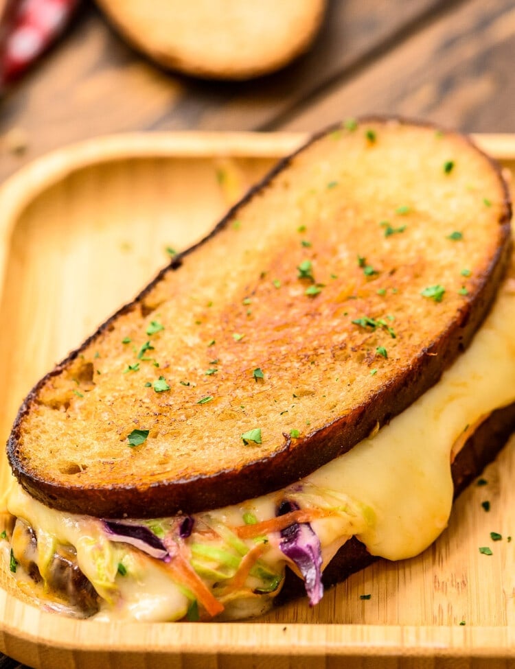 Wood platter with sandwich showing melted cheese and coleslaw