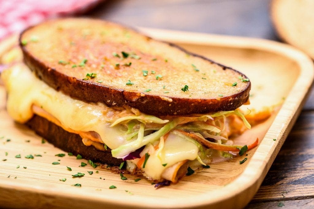 Wood plate with a rachel sandwich with melted cheese turkey and coleslaw