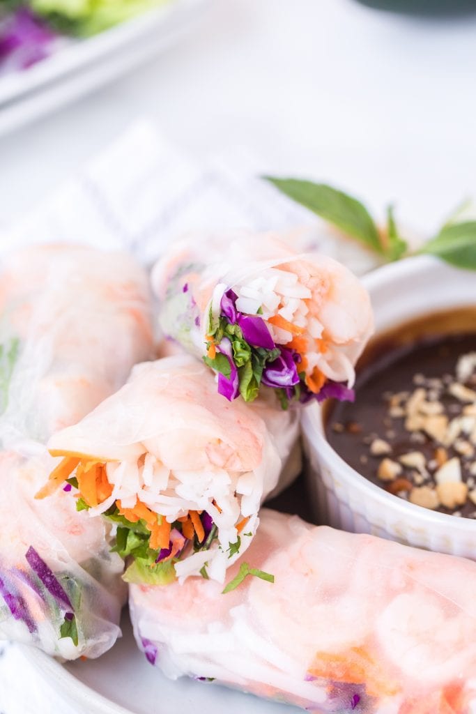 Stack of fresh spring rolls cut open on white plate next to peanut sauce in bowl