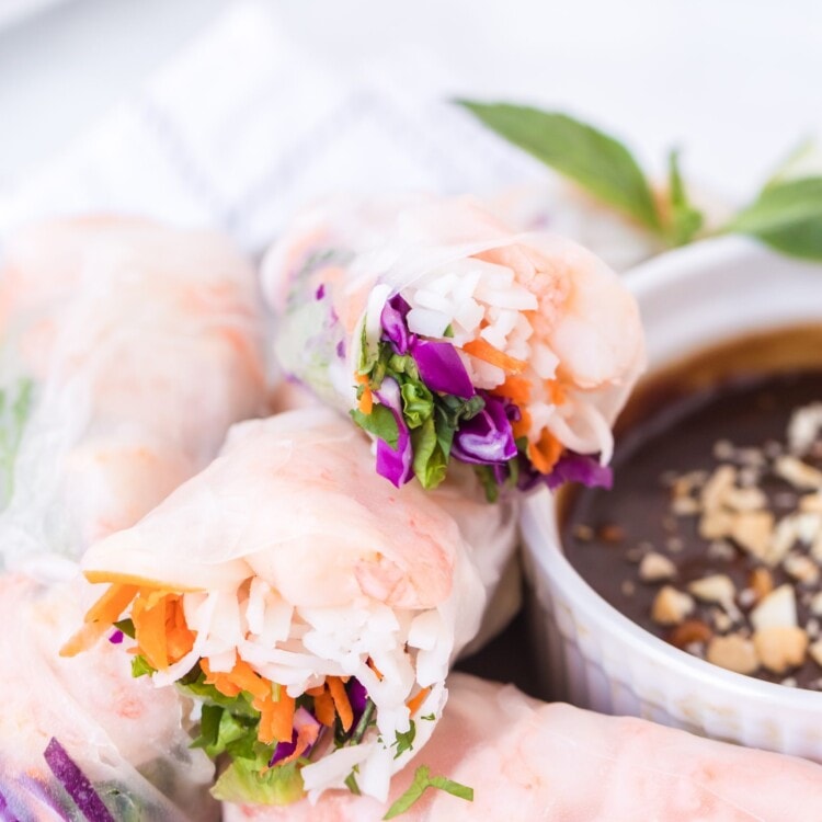 Stack of fresh spring rolls cut open on white plate next to peanut sauce in bowl