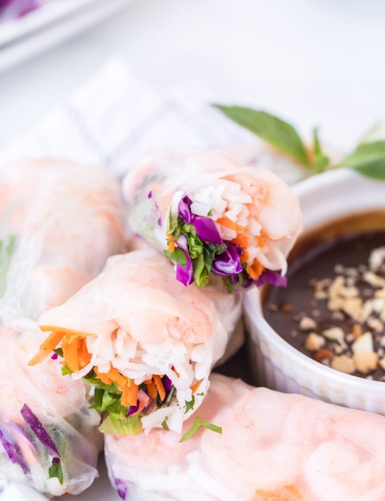 Stack of fresh spring rolls cut open on white plate next to peanut sauce in bowl