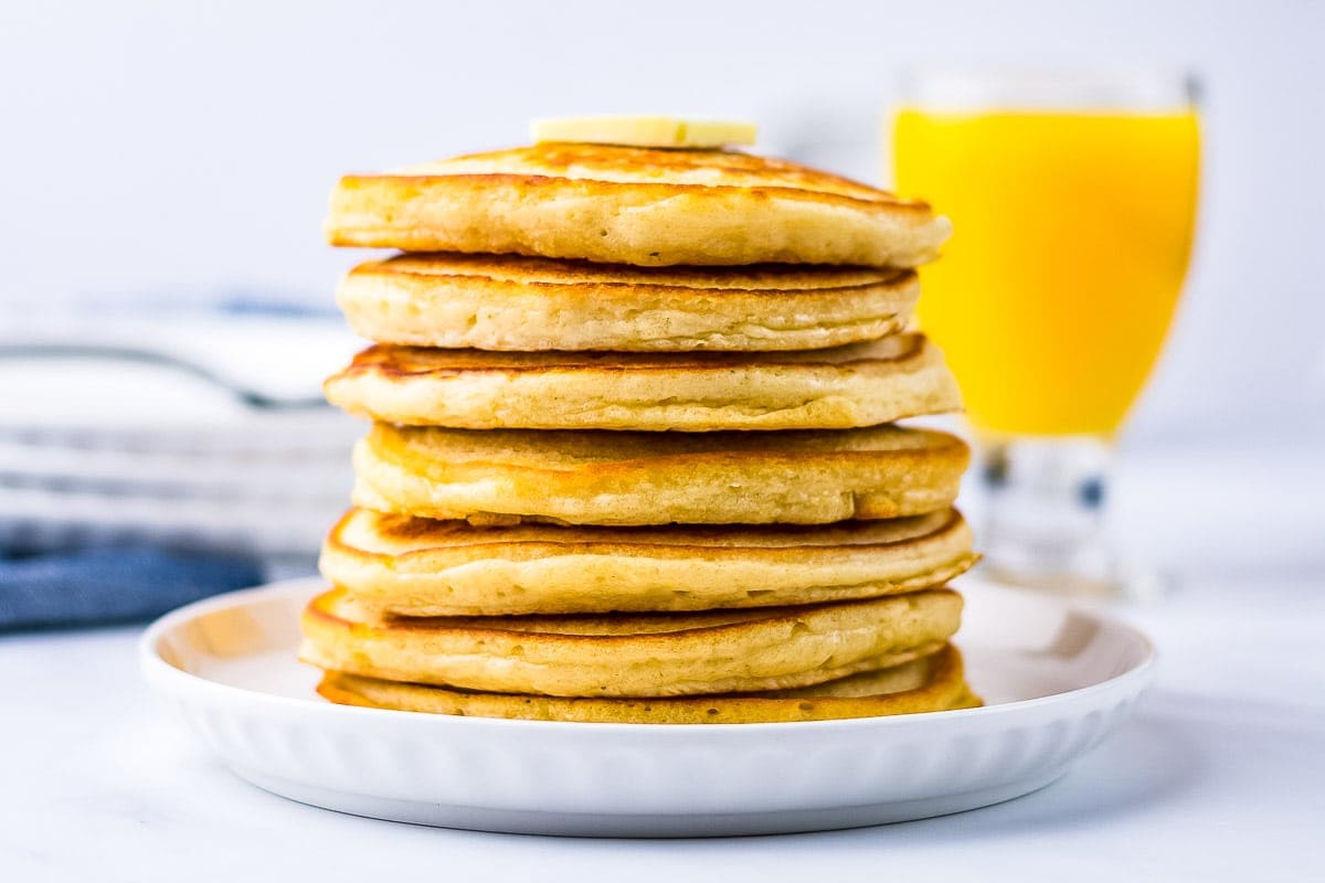 White plate with stack of pancake orange juice glass in background