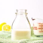 Glass bottle with milk in it on green check napkin and lemons in background