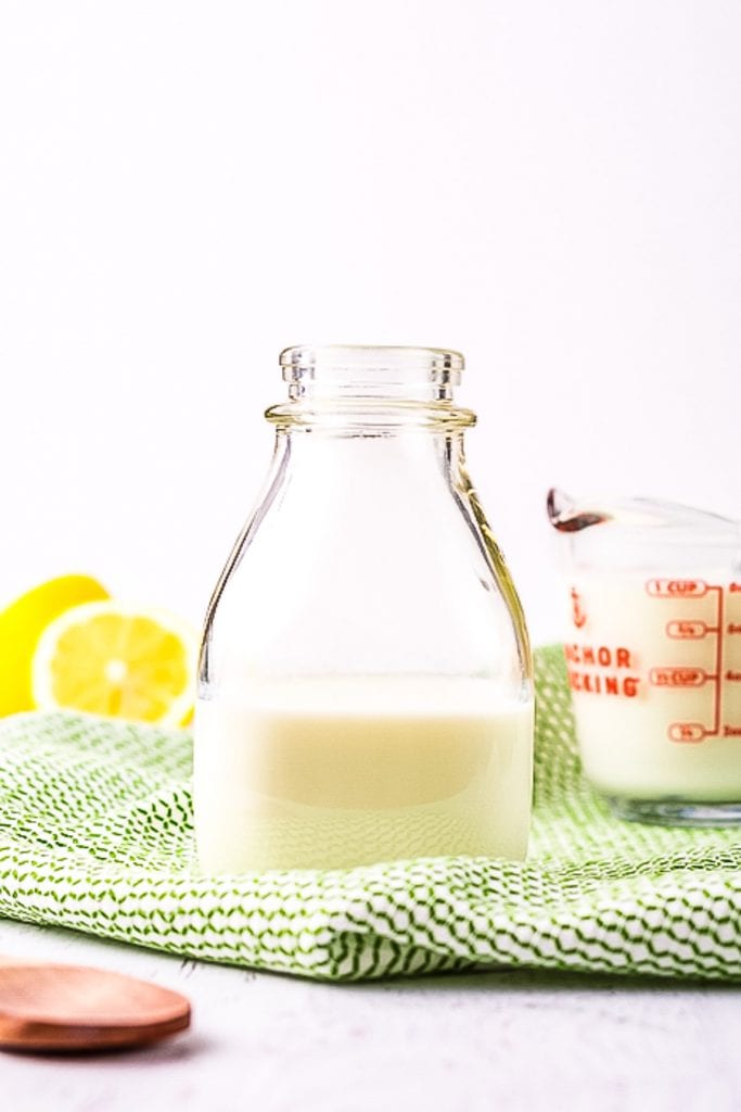 Glass bottle with milk in it on green check napkin and lemons in background