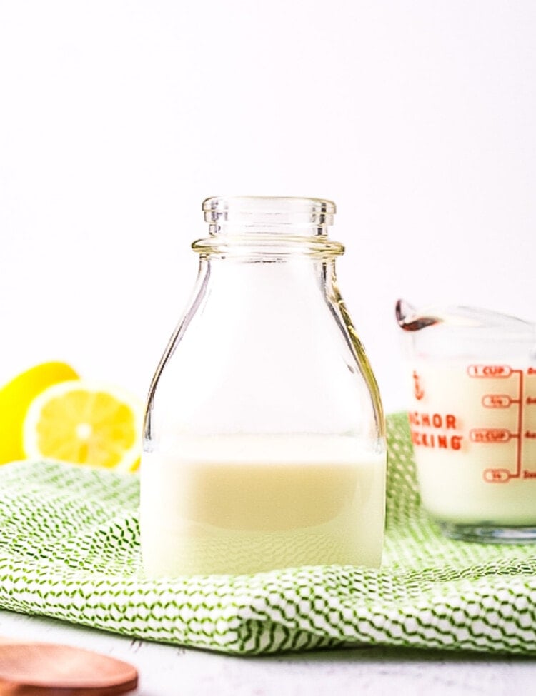 Glass bottle with milk in it on green check napkin and lemons in background