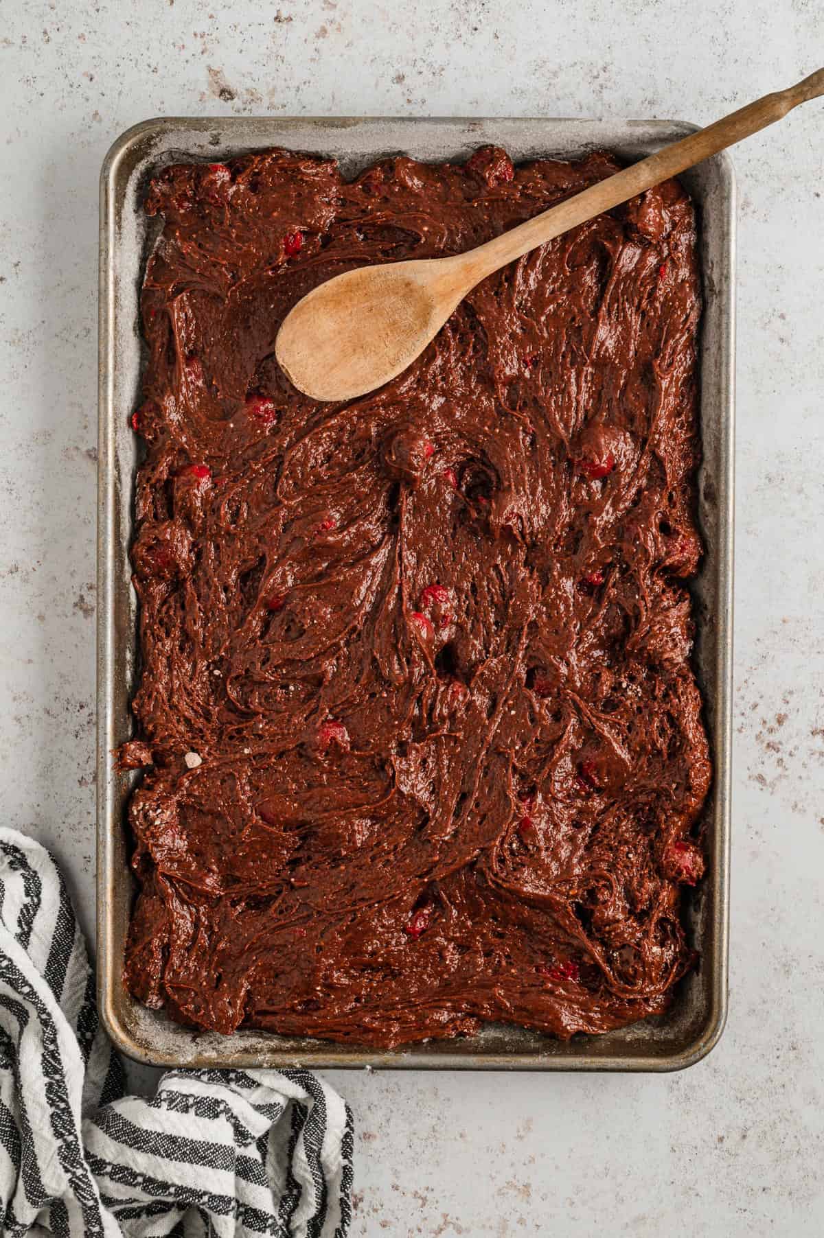 Spreading Chocolate Cherry Bars batter in baking sheet using a wooden spoon