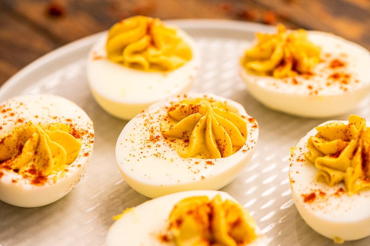 Hard boiled eggs sliced in half with deviled egg filling piped into them and garnish with paprika on plate