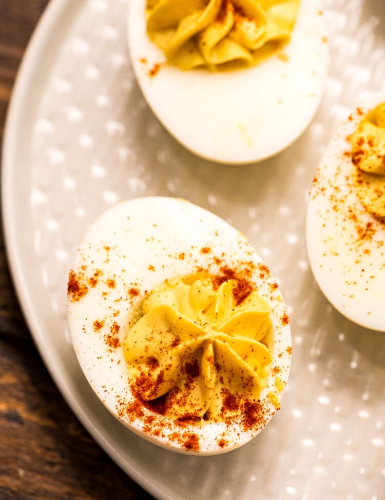 Overhead image of off white plate with deviled eggs garnished with paprika on it