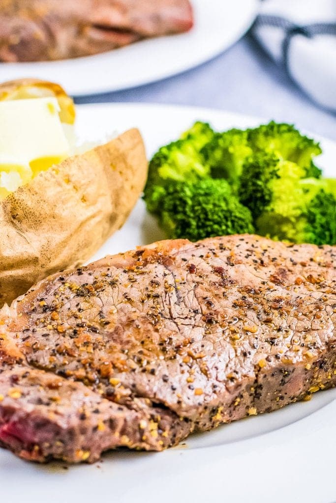 Plate with seasoned steak on it with steamed broccoli and baked potato