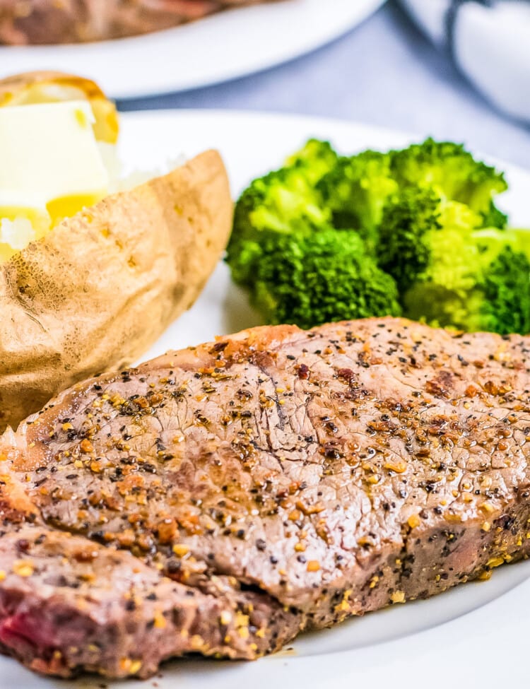 Plate with seasoned steak on it with steamed broccoli and baked potato