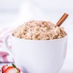 Bowl of rice pudding with cinnamon stick in it and strawberry next to bowl