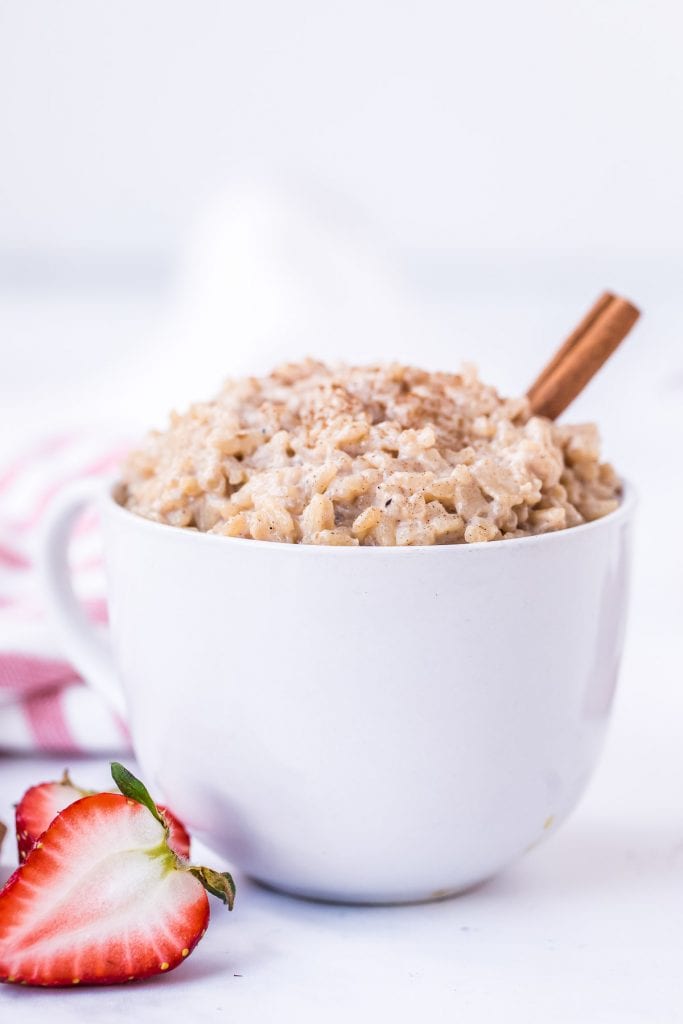 Bowl of rice pudding with cinnamon stick in it and strawberry next to bowl