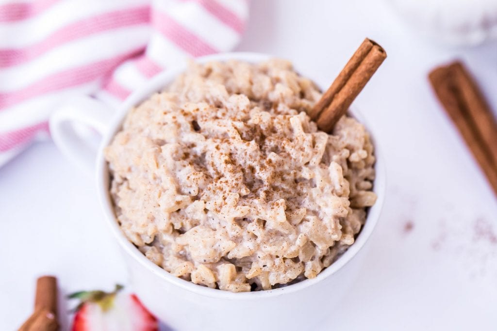 Overhead image of a white bowl of rice pudding garnished with ground cinnamon and a cinnamon stick