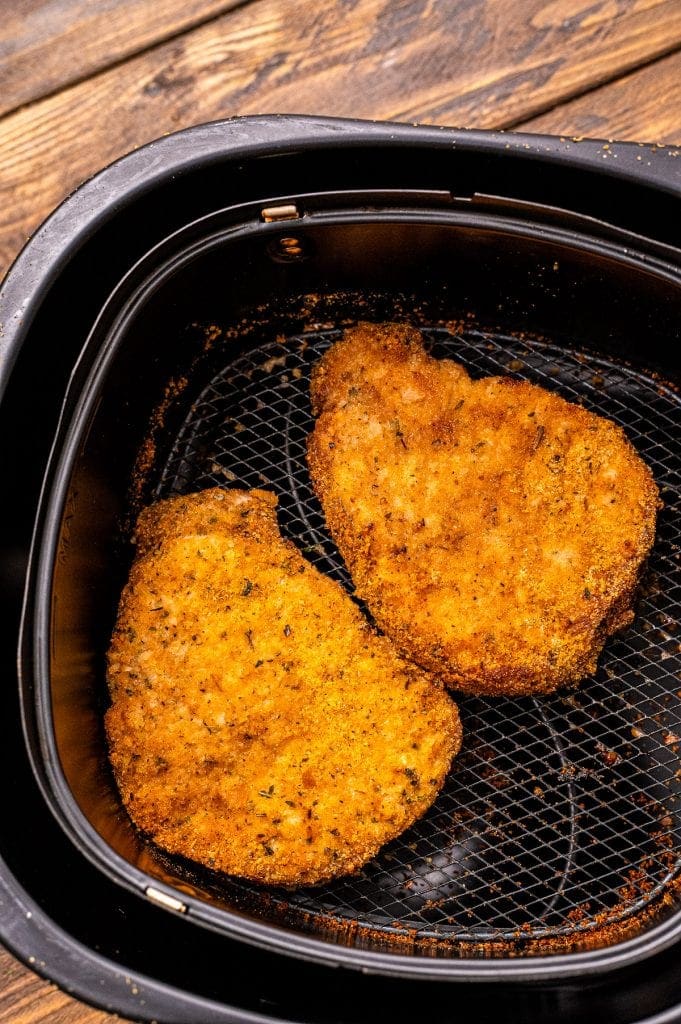 Air fryer basket with two breaded pork chops in it