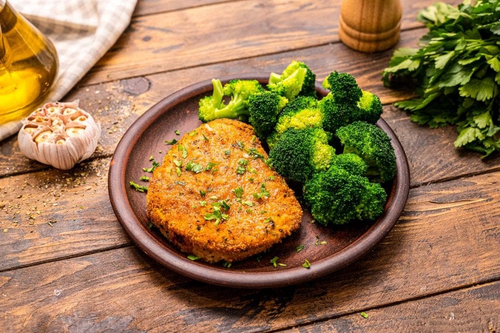 Brown wooden plate with pork chop and steamed broccoli on it