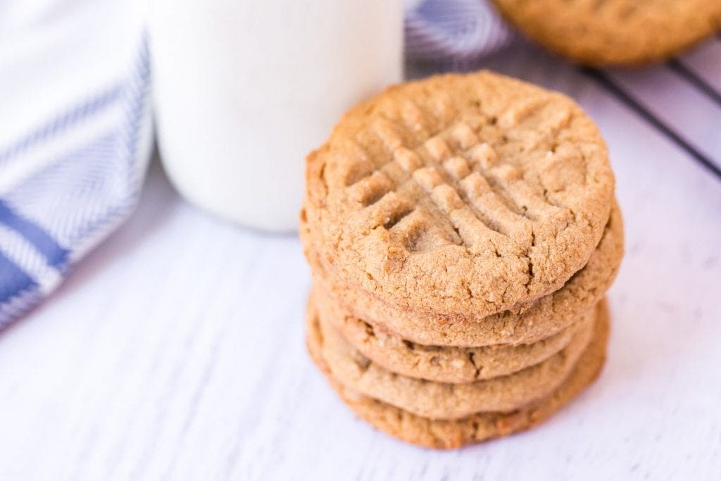 White background with a stack of cookies and jar of milk in background with blue and white napkin