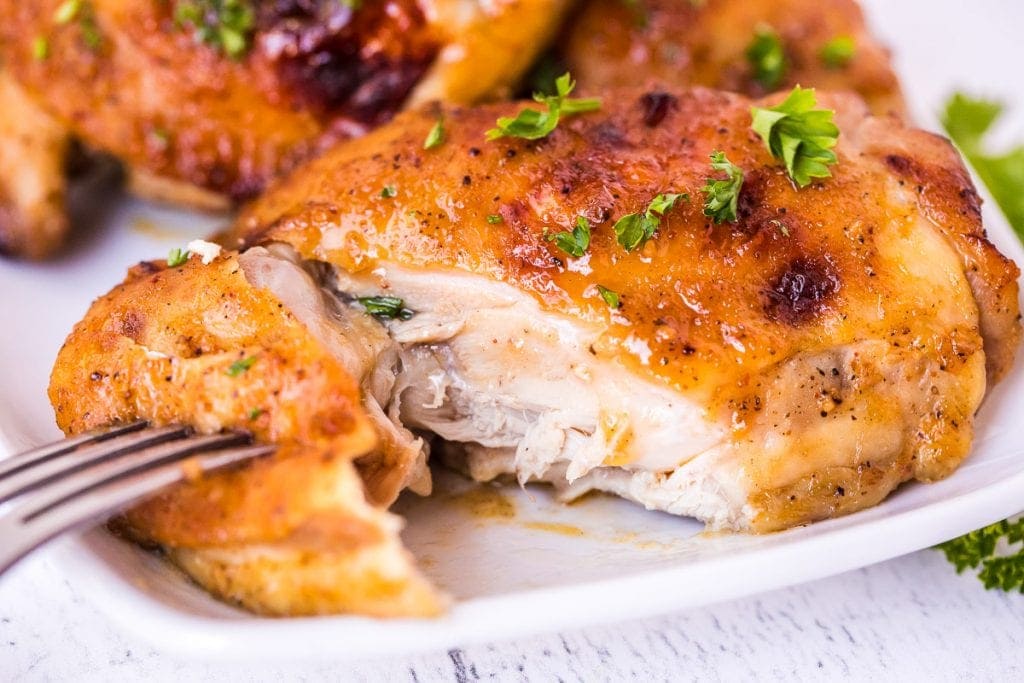 Fork pulling a piece of cut chicken thigh away from the rest of it on white plate