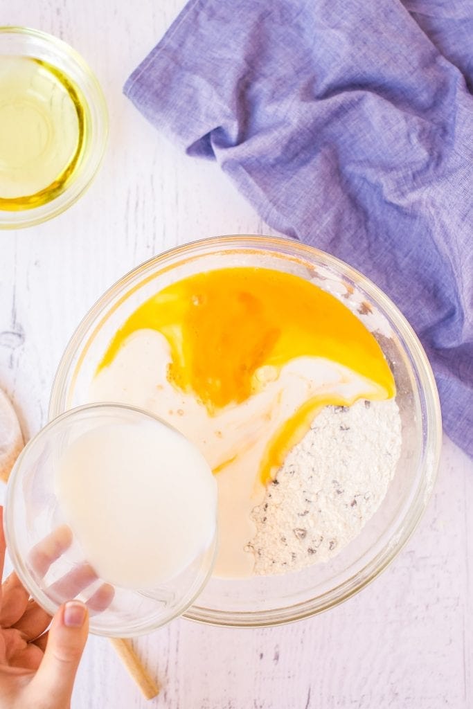 Adding milk to ingredients for chocolate chip muffins in glass bowl