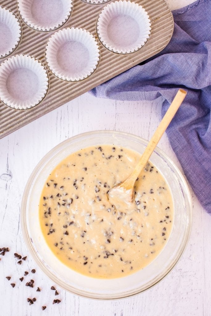 Wooden spoon in muffin batter in glass bowl with muffin tin in background