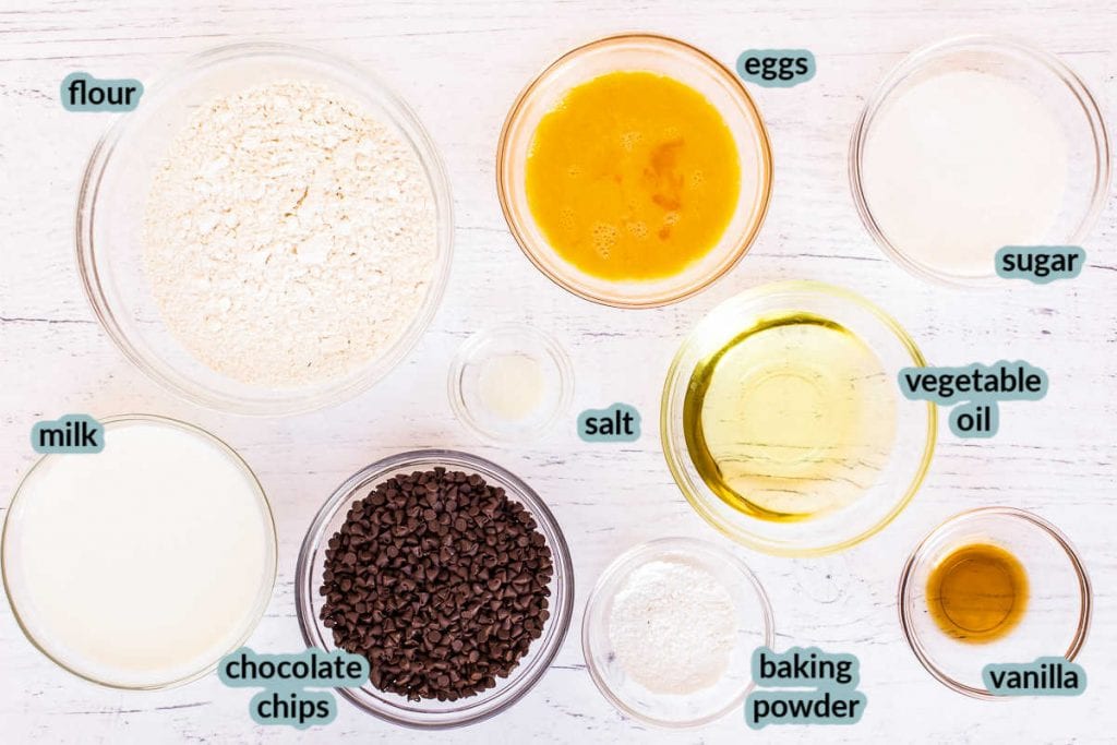 Ingredients for muffins in clear bowls on white background like flour sugar eggs chocoalte chips and more