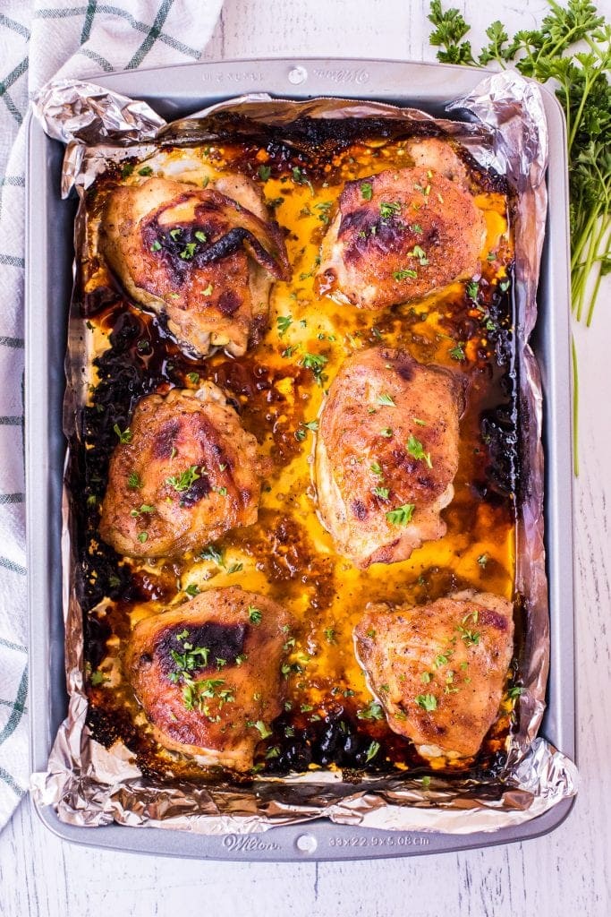 Sheet pan covered in foil with baked chicken thighs on it. Overhead image showing baked chicken.