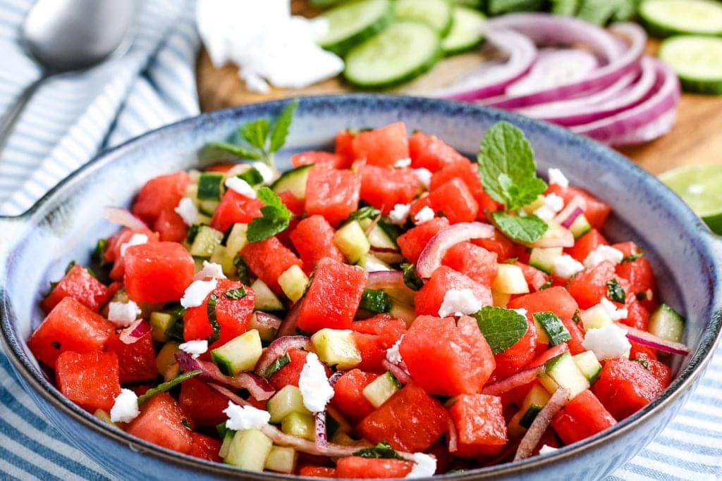 Blue bowl with prepared watermelon salad on top of blue and white striped napkin.