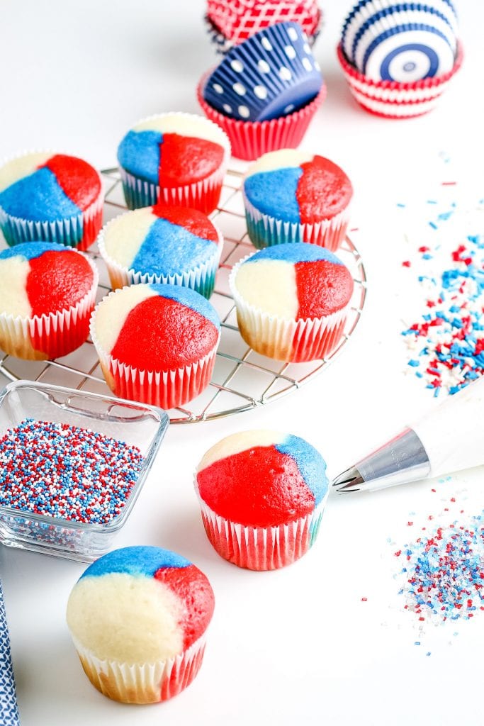 Red, white and blue cupcakes with sprinkles spread out on white background.
