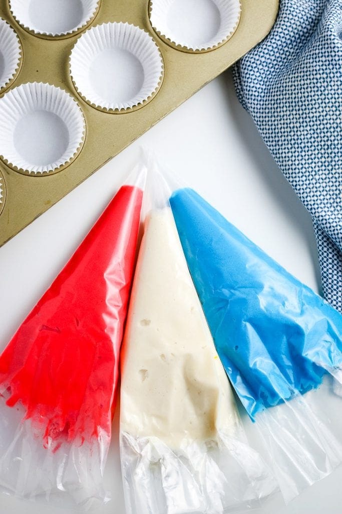 Overhead image of three bags filled with red, white and blue cake mix in it with a muffin tin and white liners in it behind it.