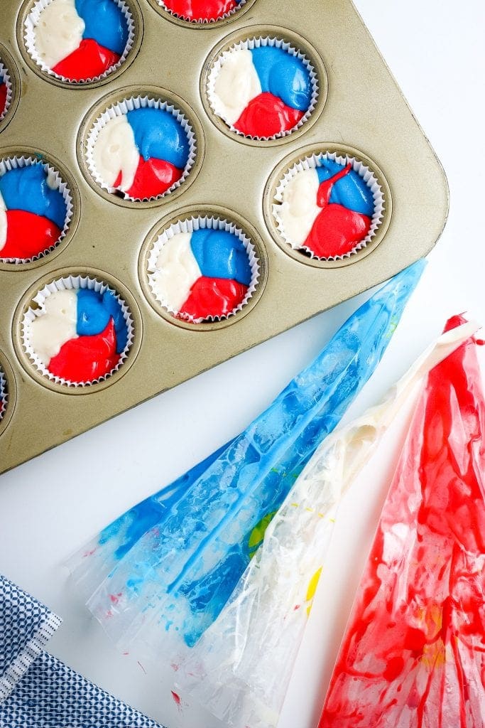 Overhead image of muffin tin with white cupcake liners filled with red, white and blue batter.