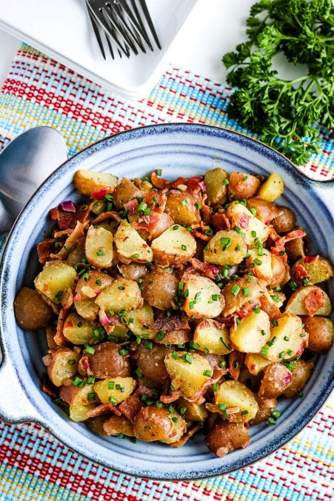 Overhead image of blue bowl with german potato salad in it on a napkin with silverware