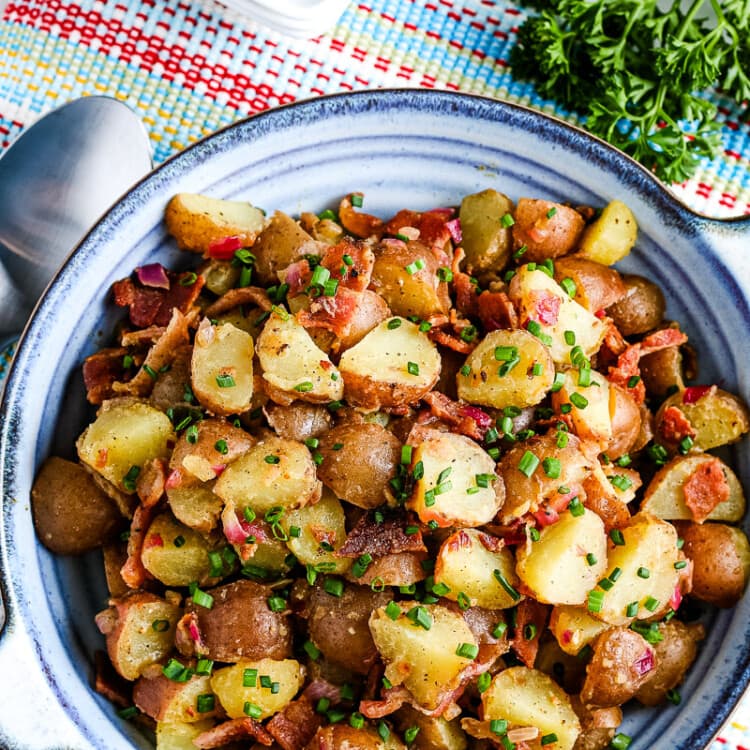 Overhead image of blue bowl with german potato salad in it on a napkin with silverware