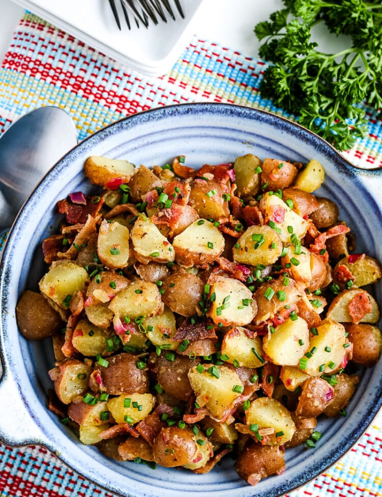 Overhead image of blue bowl with german potato salad in it on a napkin with silverware