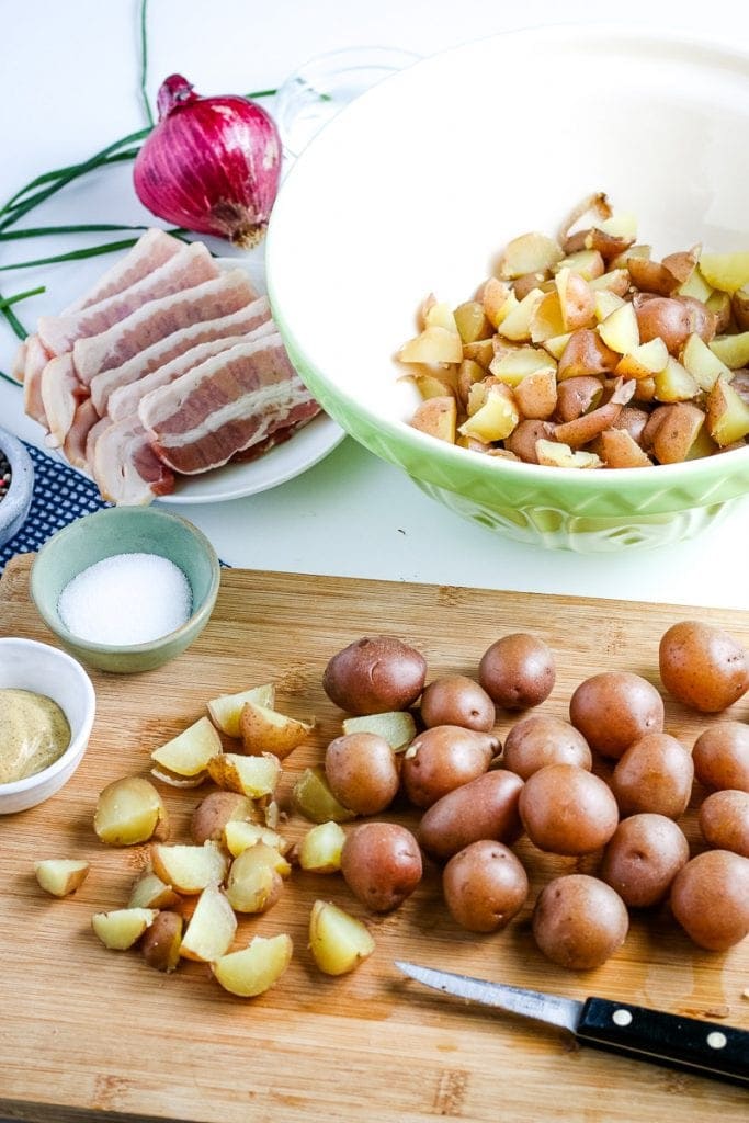 Cutting board with cooked red potatoes being cut into pieces