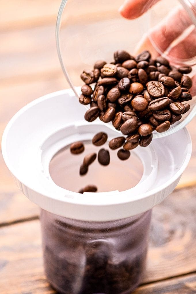 Coffee beans being poured into a coffee grinder with a white top