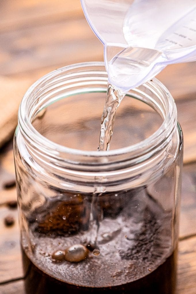 Water being poured into a glass jar with ground coffee.