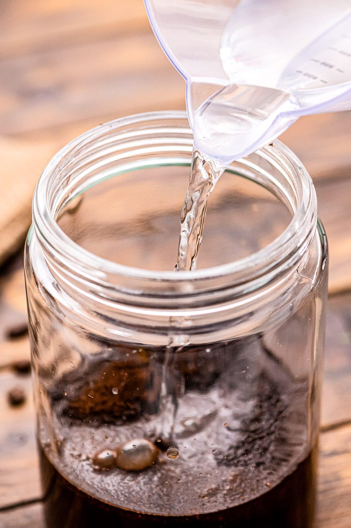 Water being poured into a glass jar with ground coffee.