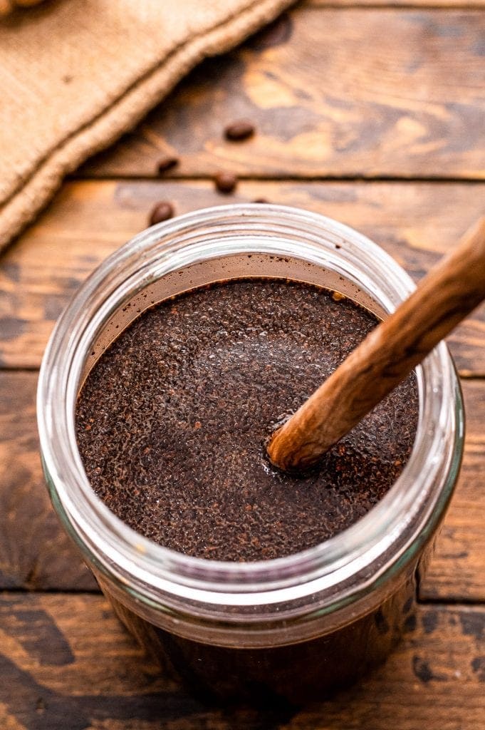 Wooden spoon stiring water and coffee grounds together in glass jar.