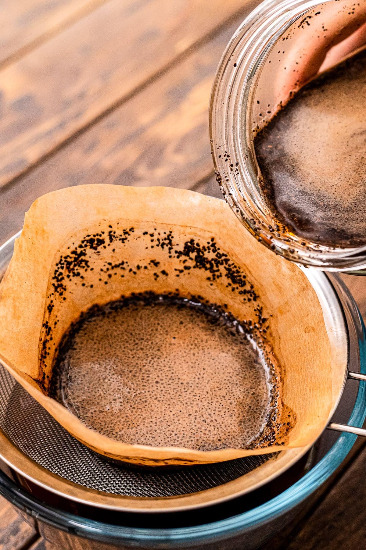 Pouring cold brewed coffee through coffee filter into glass jar to strain the coffee grounds.