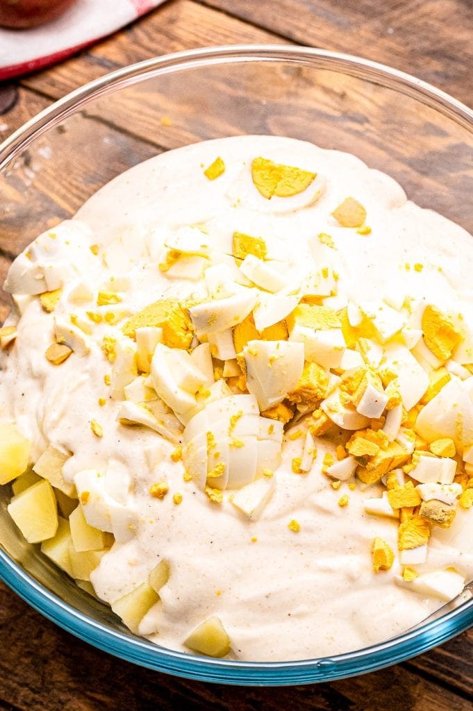 Glass bowl with potato salad dressing, hard boiled eggs that are diced and potatoes before mixing togther.