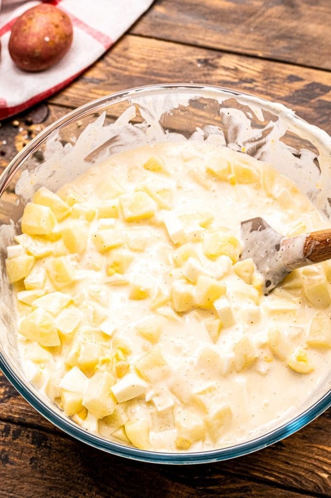 Glass bowl with potato salad ingredients being mixed together with spatula