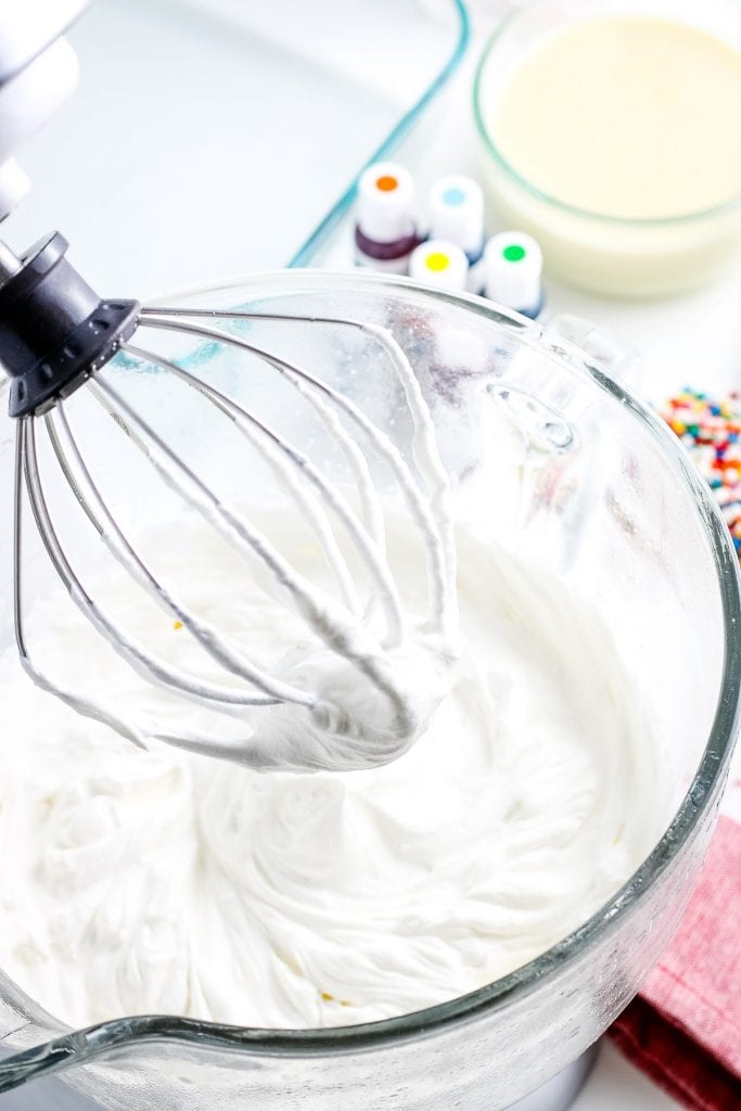 Stand mixer with whisk attached and whipped cream in bowl with stiff peaks