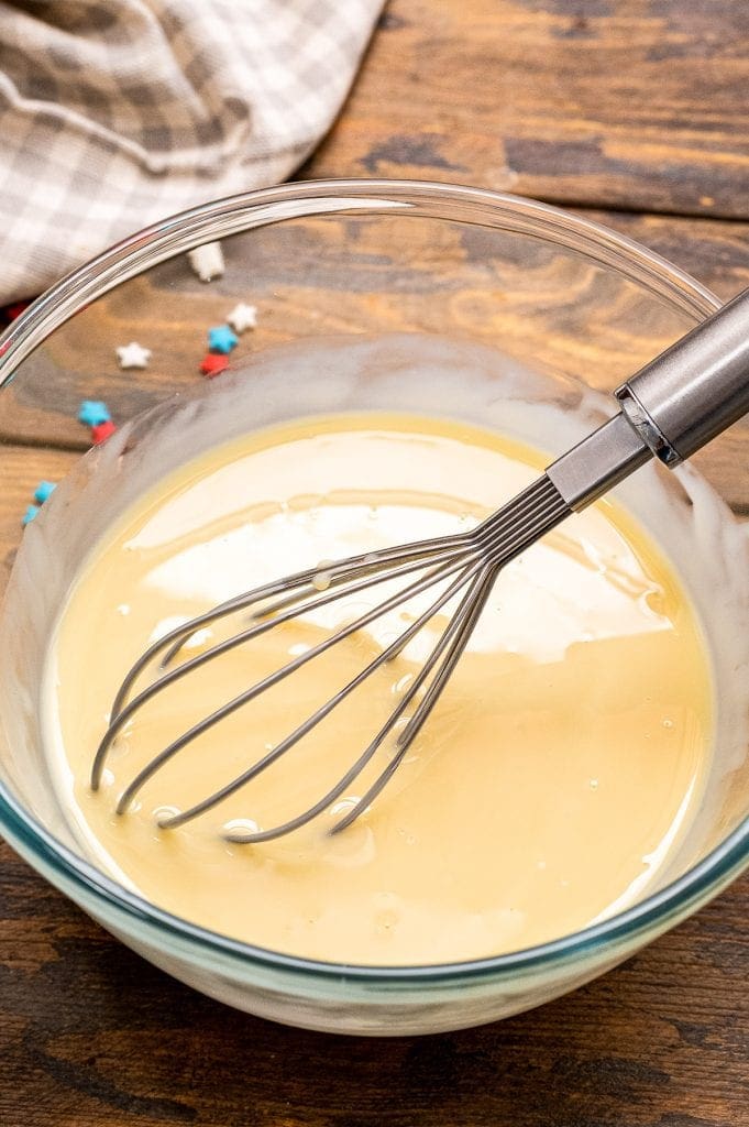 Glass bowl with whisk combining sweetened condensed milk and vanilla
